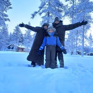 Ravi and his family posing happily in the snow at a husky farm during their Finland northern lights tours.