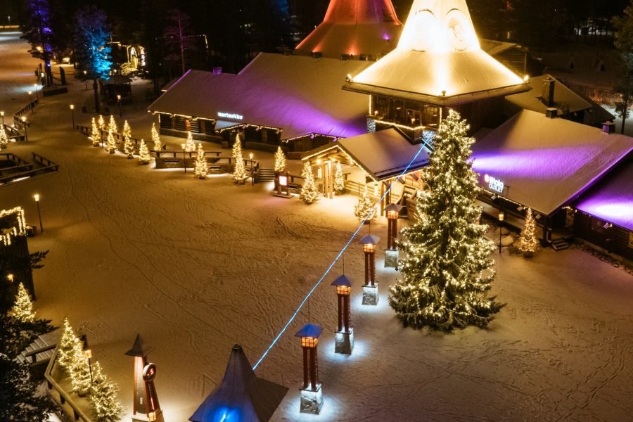 Aerial view of Santa Claus Village in Rovaniemi at night with glowing lights, snowy rooftops, and festive atmosphere.