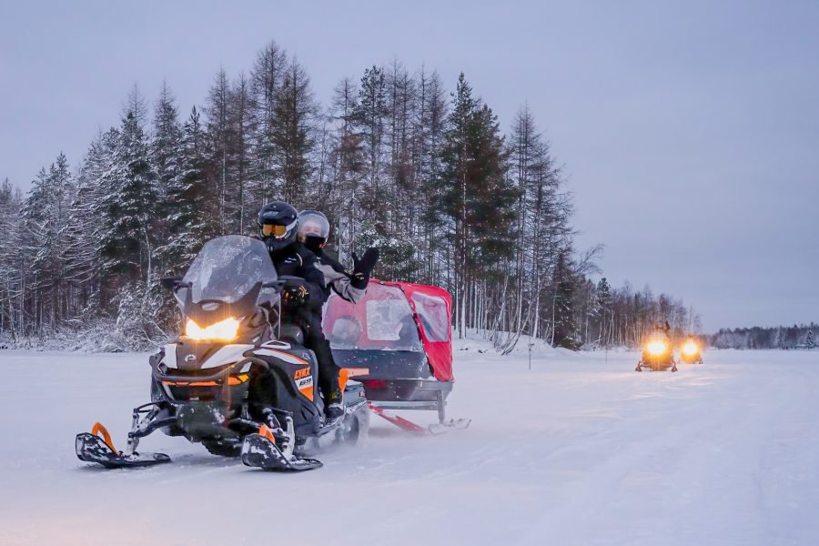 Snowmobile Safari with kids seated in a sledge behind in a snowy Arctic landscape during the 14 Days Iceland, Norway and Finland tour package.