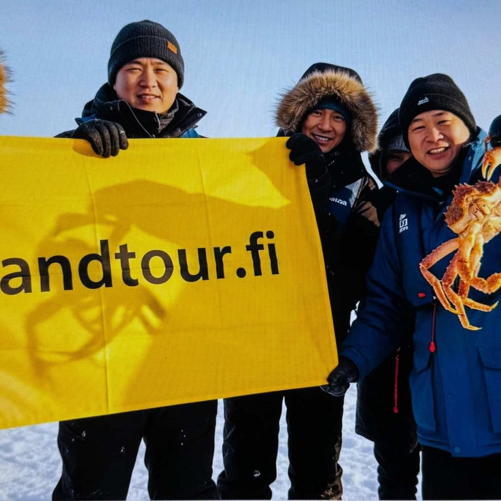 Travelers enjoying a King Crab Safari in Kirkenes during the 14 days Finland tour from Singapore, holding freshly caught giant crabs in the snow.