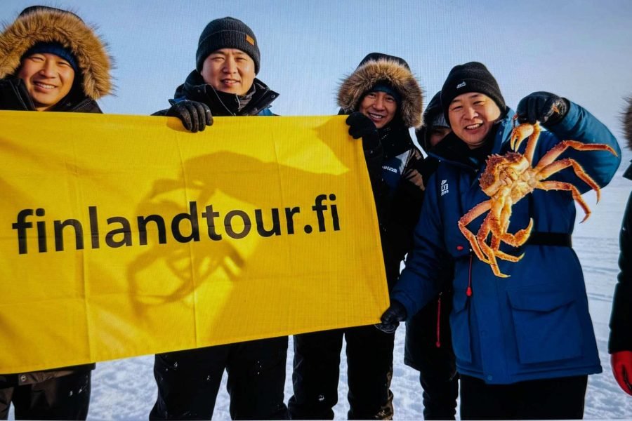 Travelers enjoying a King Crab Safari in Kirkenes during the 14 days Finland tour from Singapore, holding freshly caught giant crabs in the snow.