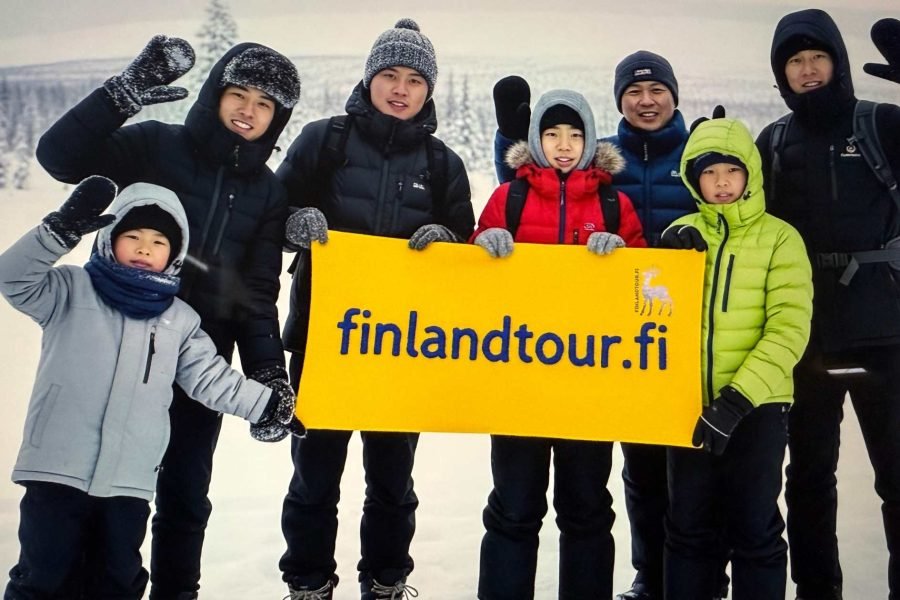 Group of happy travelers posing in snowy Finland after booking their 7 days Finland tour from Singapore with finlandtour.fi