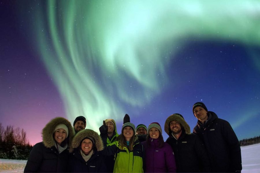Travelers posing under the vibrant Northern Lights during the 10D/9N Helsinki, Ivalo, Rovaniemi, Kiruna, Tromso, and Oslo tour, capturing magical Arctic moments.